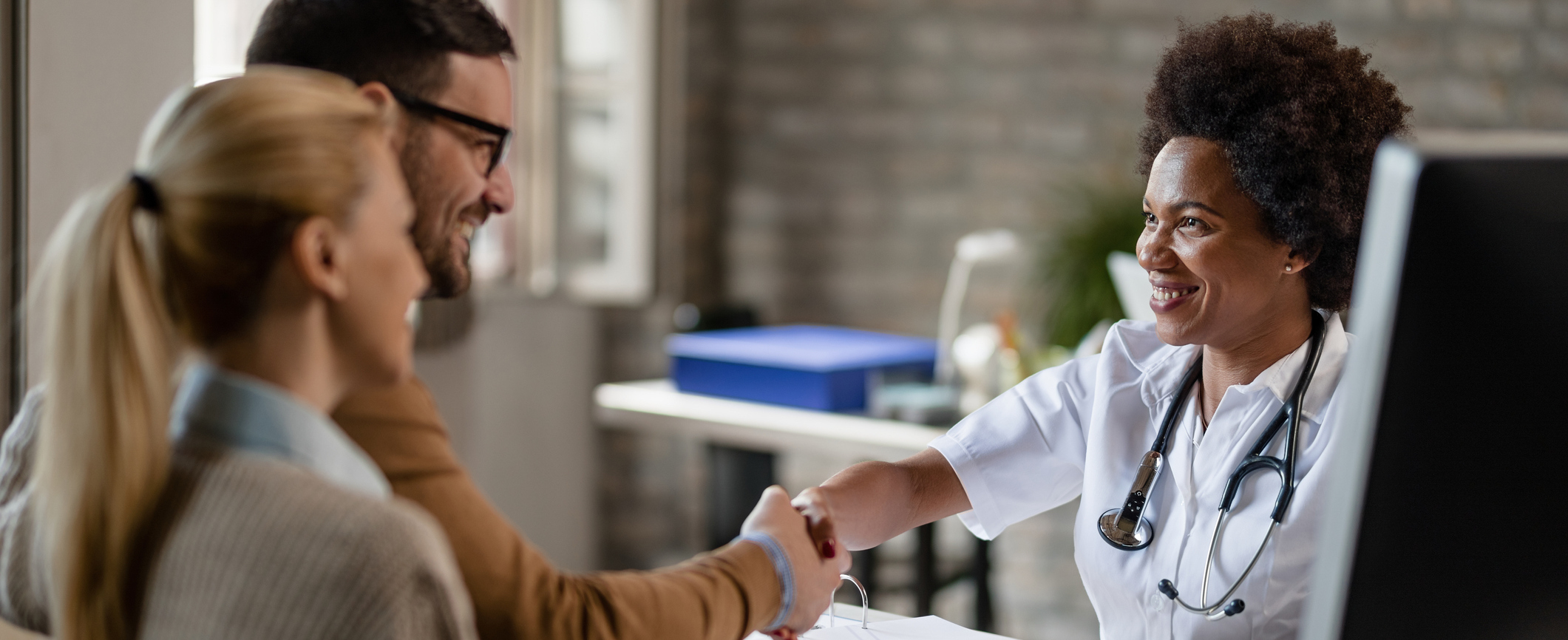 Happy African American doctor greeting a couple at medical clinic.