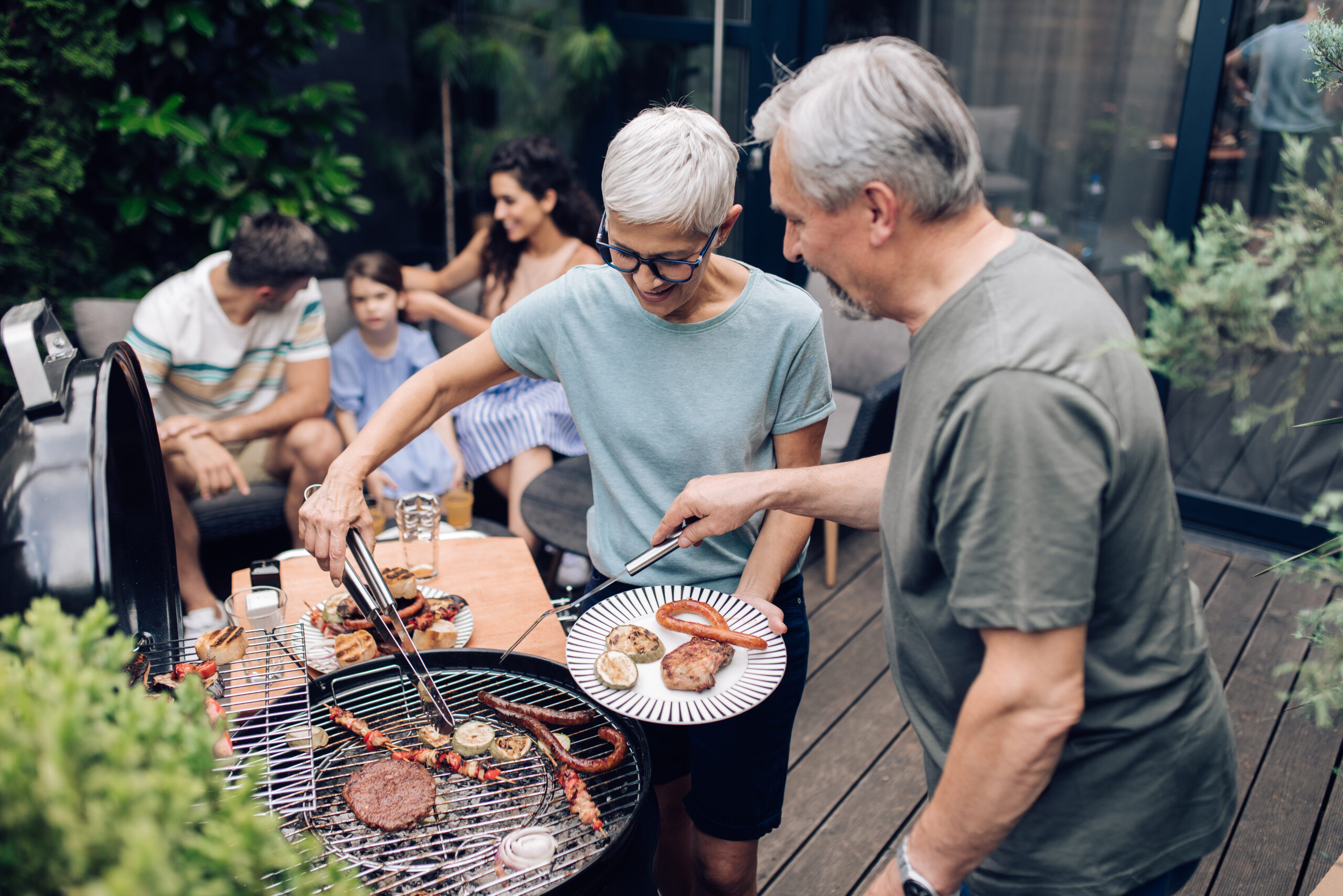 Senior couple grilling on a deck with family in the background