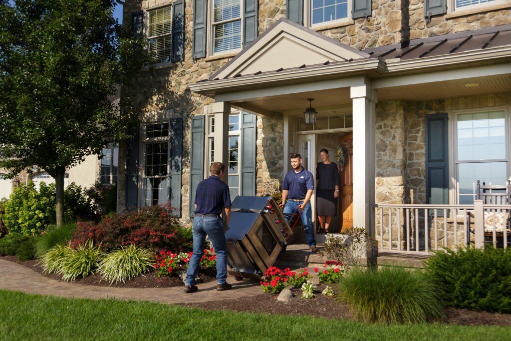 Two men pushing a dolly with a range on the front porch of a house