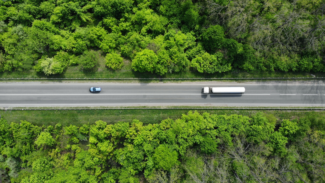 Aerial. Gasoline fuel truck driving by the highway road between green forest. Top view.