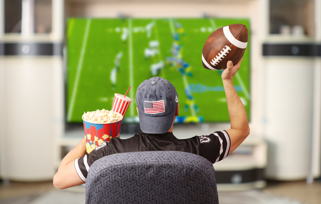 Fan of american football. Man with a ball watching TV.