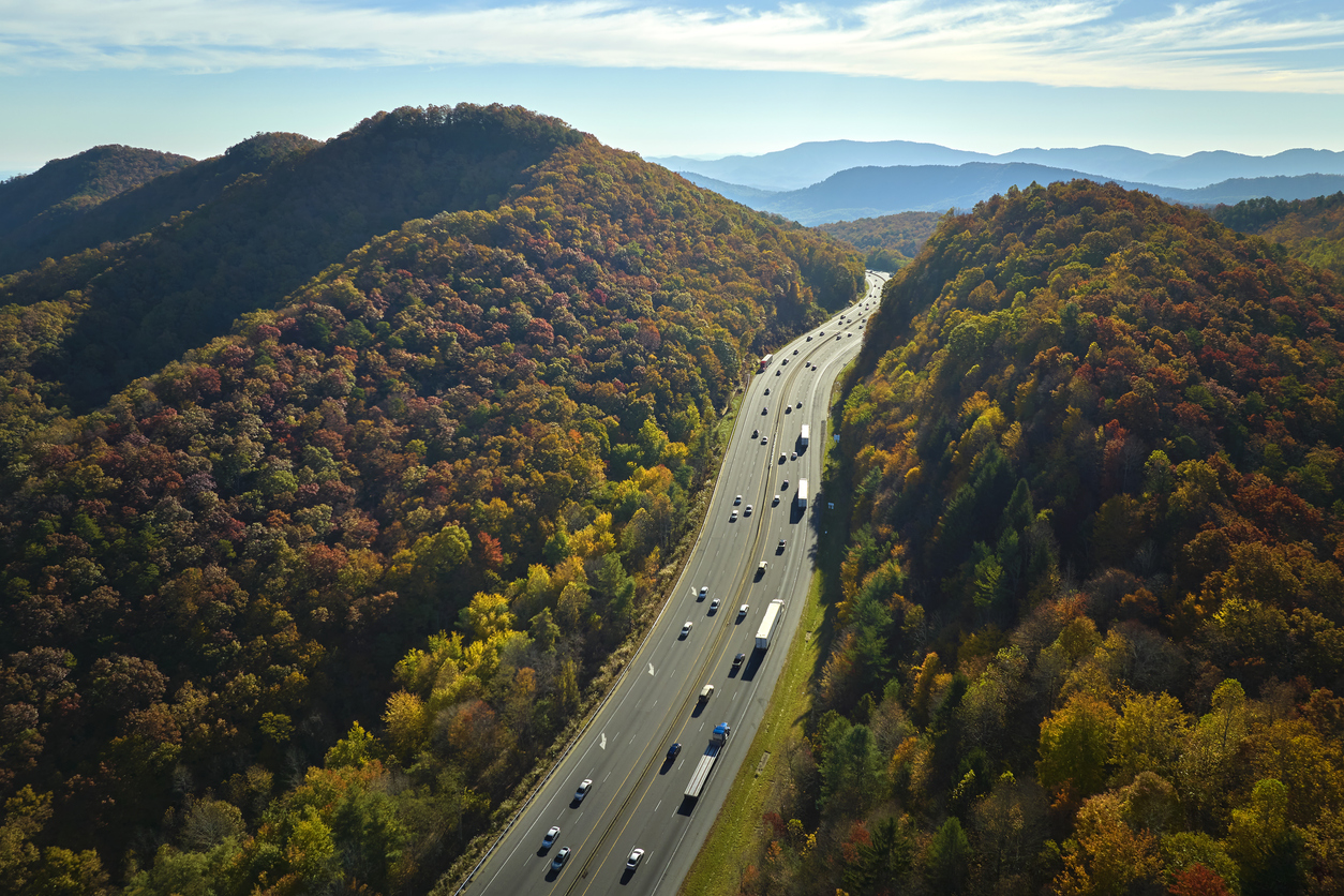 View from above of I-40 freeway in North Carolina heading to Asheville through Appalachian mountains in golden fall season with fast driving trucks and cars. Interstate transportation concept.